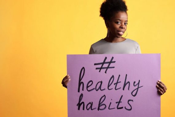 Portrait of a woman holding a healthy habits sign, set against a vibrant yellow background.